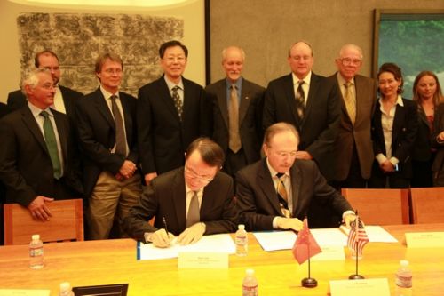two seated men signing documents, flanked by several officials standing behind them