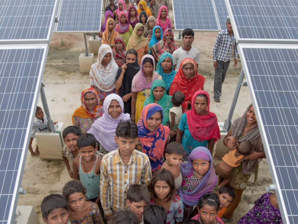 Group of children, youth, and women stand smiling beneath solar panels in India